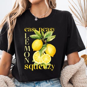 May include: Black t-shirt with a yellow lemon graphic and the text "easy peasy lemons squeezy". The graphic features whole and sliced lemons with green leaves. The shirt is a casual style.
