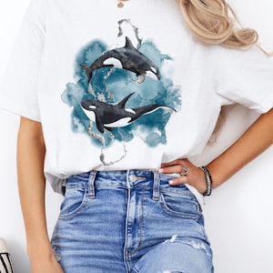 May include: White t-shirt with a watercolor design of two orcas swimming in blue water.