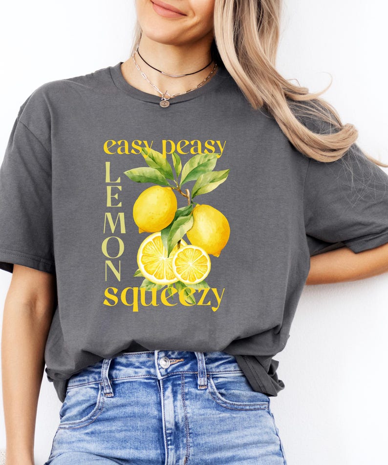 May include: A dark gray t-shirt featuring a yellow lemon graphic with the words "easy peasy lemon squeezy". The graphic includes yellow lemons and green leaves. The shirt is a casual style.