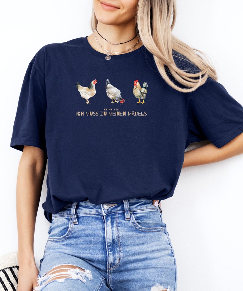 May include: A navy blue t-shirt with a graphic of three chickens. The text "Keine Zeit, ich muss zu meinen M&auml;dels" is printed on the shirt.