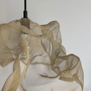 Close-up of a sand-colored wire mesh lampshade, showcasing intricate design and texture.