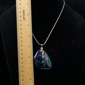 May include: A silver chain necklace with a pendant made from a dark blue and green stone. The stone is about 2 inches long and 1.5 inches wide.