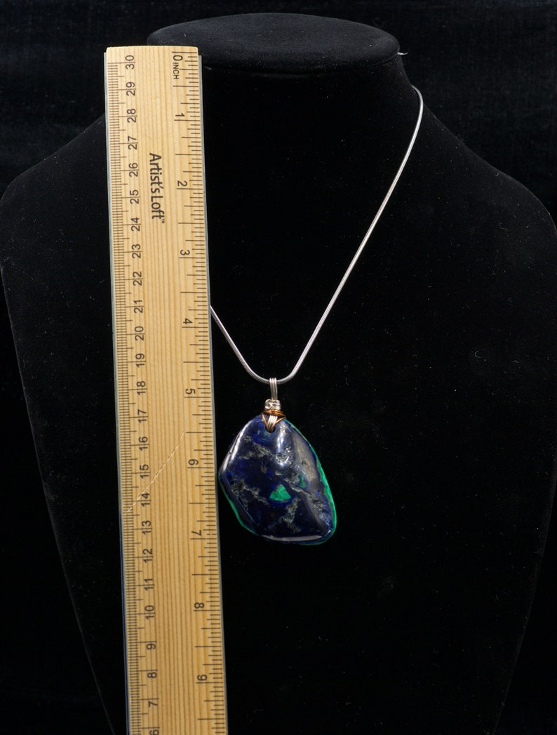 May include: A silver chain necklace with a pendant made from a dark blue and green stone. The stone is about 2 inches long and 1.5 inches wide.