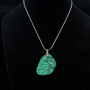 May include: A silver chain necklace with a green and blue stone pendant. The stone is irregularly shaped and has a rough texture.