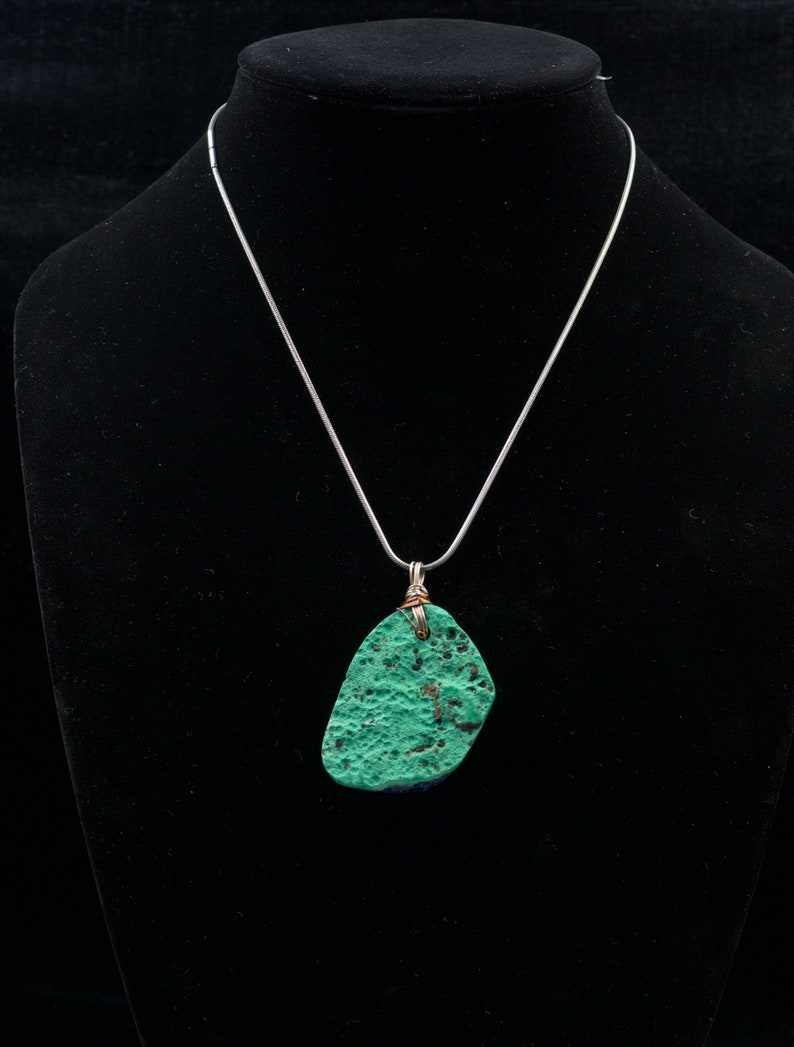 May include: A silver chain necklace with a green and blue stone pendant. The stone is irregularly shaped and has a rough texture.