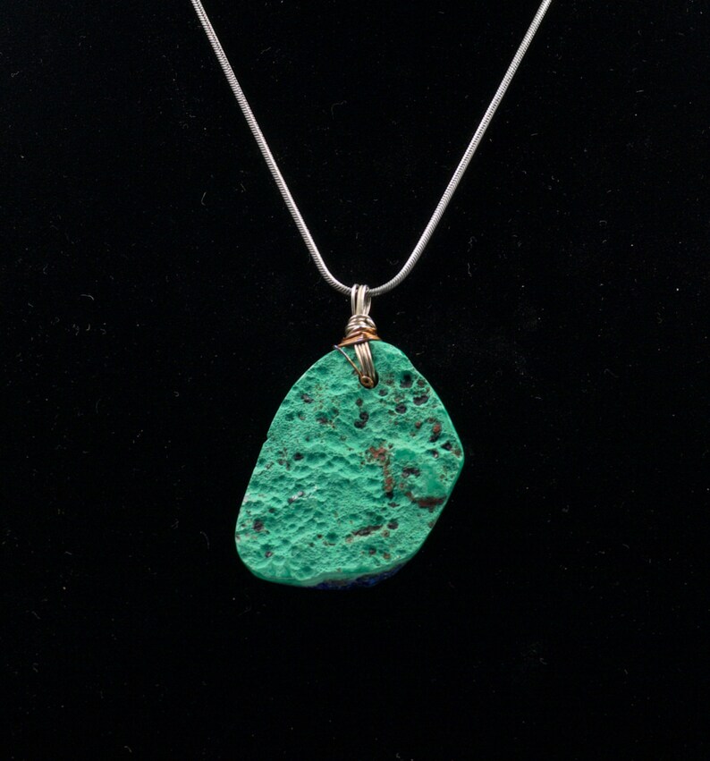 May include: A silver chain necklace with a green and blue stone pendant. The stone has a rough, textured surface.