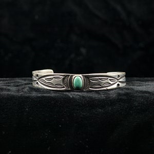 May include: A silver bracelet with a turquoise stone set in the centre. The bracelet has a geometric design with repeating patterns.