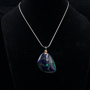 May include: A silver chain necklace with a dark blue and green stone pendant. The stone is irregularly shaped and has a rough texture.
