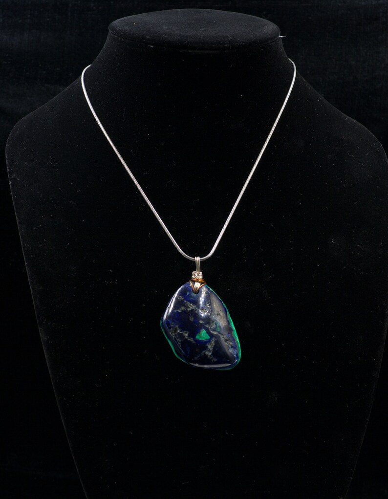 May include: A silver chain necklace with a dark blue and green stone pendant. The stone is irregularly shaped and has a rough texture.