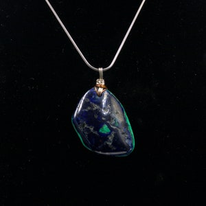 May include: A silver chain necklace with a dark blue and green gemstone pendant. The pendant is wrapped in copper wire.