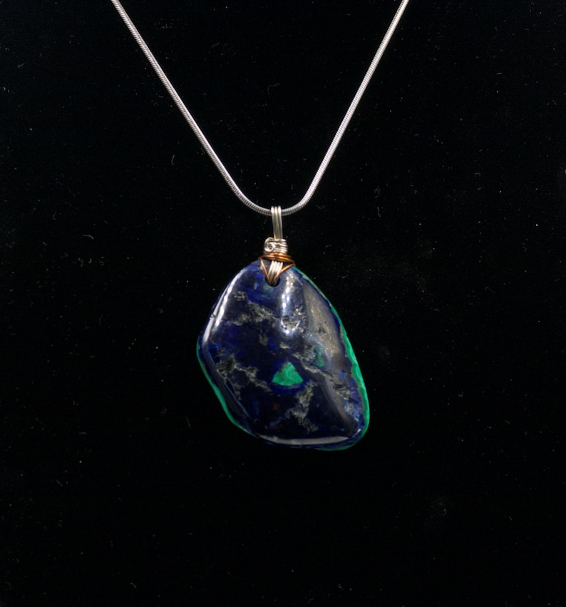 May include: A silver chain necklace with a dark blue and green gemstone pendant. The pendant is wrapped in copper wire.