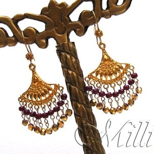 以下が含まれることがあります： 扇形のデザインと、下からぶら下がっているワインレッドのビーズが付いたゴールドのイヤリング