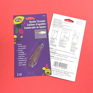 May include: A LoRan needle threader in purple packaging with a clear plastic blister pack. The front displays the product name, instructions, and a small diagram. The back shows step-by-step illustrations, a barcode, and safety warnings.