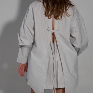 May include: A white and gray striped shirt with a long sleeve and a tie at the back.