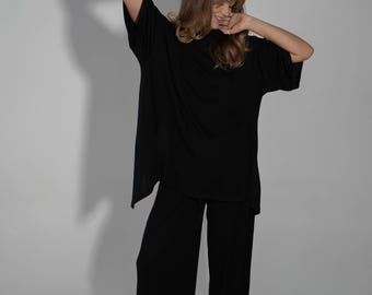 May include: A woman wearing a black oversized top and matching wide-leg pants. The top has a relaxed fit and a slightly longer length. The pants have a straight leg and a comfortable fit.