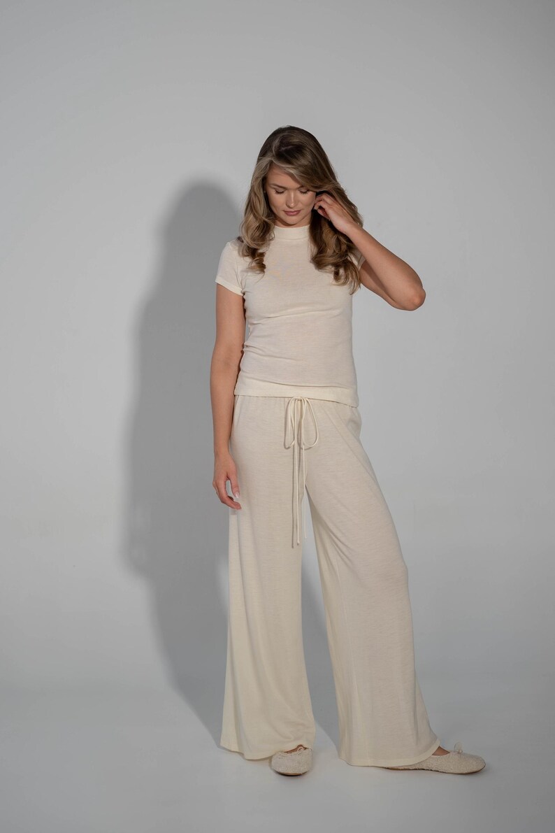 May include: A woman is wearing a cream-colored, short-sleeved top and matching wide-leg pants. The pants have a drawstring waist.