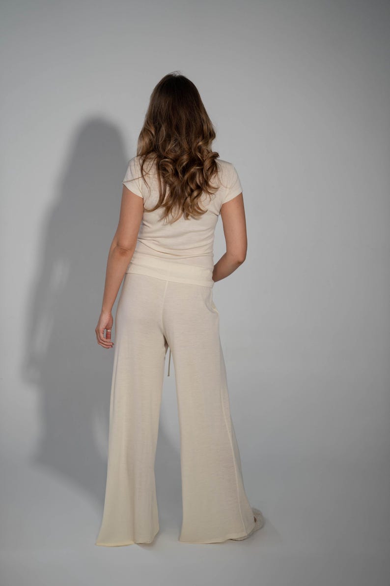 May include: A woman wearing a cream-colored top and wide-leg pants. The pants have a drawstring waist and a relaxed fit.