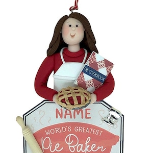 May include: A personalized ornament featuring a woman holding a pie and a cookbook. The ornament is decorated with the text "World's Greatest Pie Baker" and a space for a name and year.