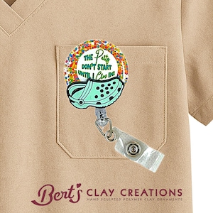 May include: A badge reel with a round design featuring the text "THE Party DON'T START UNTIL I Clog IN!" and a teal clog shoe. The reel is attached to a beige pocket.