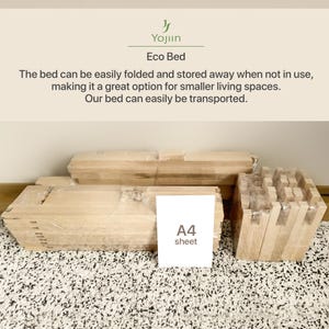 May include: An Eco Bed, disassembled and wrapped in clear plastic, ready for assembly. The wooden components are arranged on a patterned rug, with an A4 sheet for scale. The bed is designed for easy folding and storage.