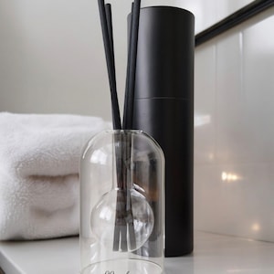May include: A clear glass diffuser with black reeds and a black cylindrical bottle. The diffuser has a round bulb at the bottom. The label on the diffuser reads "99modern".
