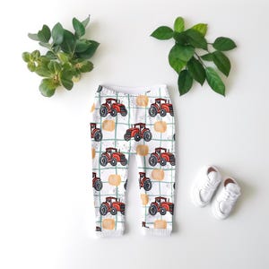 Könnte beinhalten: Weiße Baby-Leggings mit einem roten Traktor- und orangefarbenen Kürbisdruck. Die Leggings haben ein grün-weißes Karomuster.