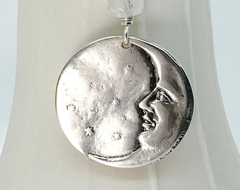 May include: A silver necklace with a crescent moon pendant and a clear crystal bead. The moon pendant has a face on it and is surrounded by stars.