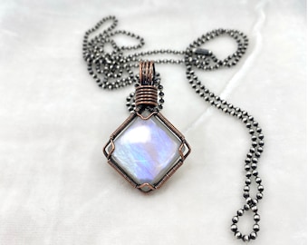 Può includere: Una collana con catena d'argento con un ciondolo avvolto in filo di rame che presenta una pietra di luna iridescente.