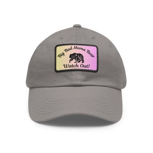 May include: A gray baseball cap with a patch that says "Big Bad Mama Bear Watch Out!" The patch has a pink and yellow gradient background and a black silhouette of a bear.