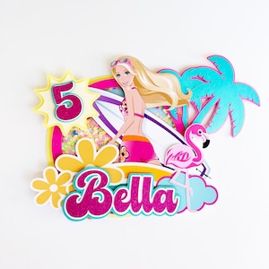 May include: A pink flamingo, a palm tree, and a surfboard with a doll wearing a pink bikini and sunglasses. The number 5 and the name Bella are also included in the design. This is a cake topper for a birthday party.