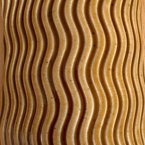 May include: A textured surface featuring a repeating pattern of vertical, parallel wavy lines in a warm, golden-brown colour. The surface has a consistent, smooth, and slightly glossy finish with subtle variations in tone across the ridges.