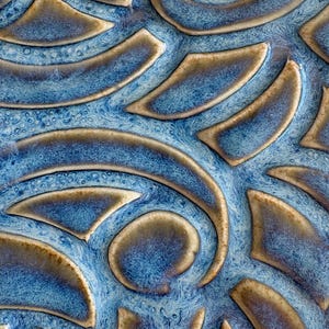 Peut inclure: Gros plan sur un carreau de céramique avec un motif abstrait texturé. Le motif présente des formes bleues et marron tourbillonnantes, créant une sensation de profondeur et de mouvement. La finition brillante rehausse les couleurs.