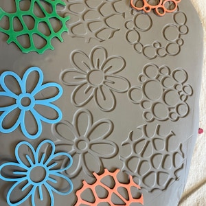 Peut inclure: Gros plan sur une surface d'argile avec différentes formes et motifs enfoncés. Les formes comprennent des fleurs, des cercles et un motif en forme de toile d'araignée. Les formes sont de différentes couleurs, notamment le vert, le bleu, l'orange et le rouge.