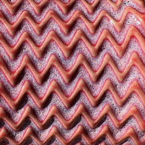 May include: Abstract, textured surface with a repeating zigzag pattern. The design features alternating bands of red and purple hues, creating a visually dynamic and tactile effect. The surface appears to have a glossy finish.