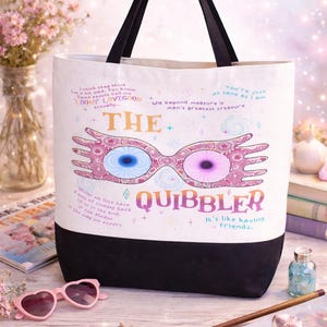 May include: White tote bag with black handles and a black bottom. The bag features a graphic of Spectrespecs glasses and the word "QUIBBLER". Text includes "It's like having friends."
