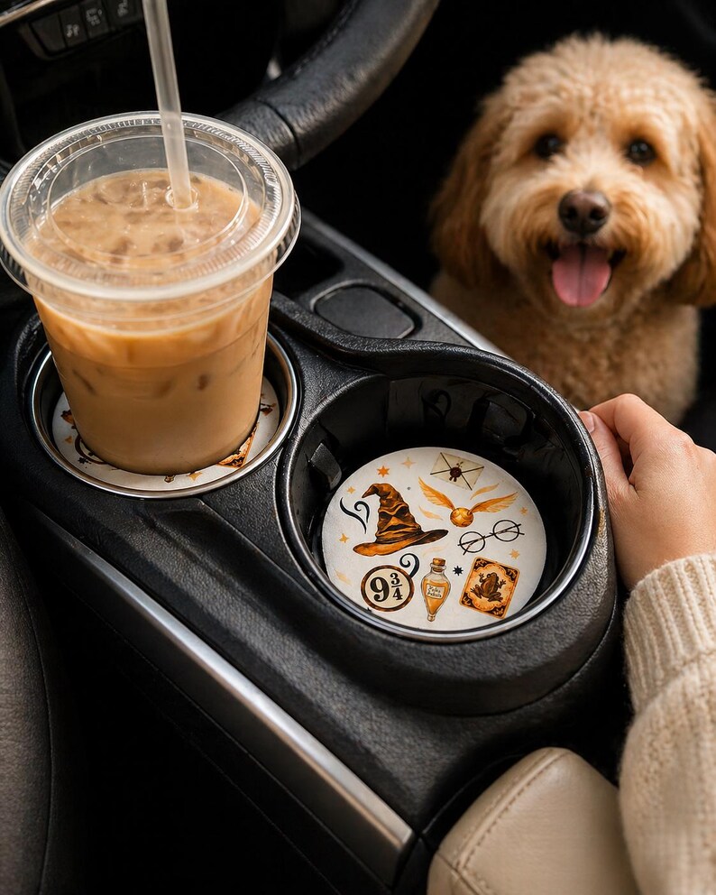 May include: A car cup holder with two coasters. One coaster has a coffee drink on top. The other coaster has a wizard hat, glasses, potion bottle, and other magical themed images. A dog is in the background.