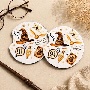 May include: Two white car coasters with a Harry Potter theme. Each coaster features a Sorting Hat, Golden Snitch, glasses, and a 9 3/4 sign. Other graphics include a potion bottle and a frog card.