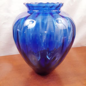 May include: A vibrant blue glass vase with a rounded body and a ruffled rim. The vase has a glossy finish and a textured, ribbed design. The color transitions from a deep indigo at the base to a lighter shade near the top.