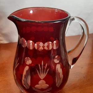 May include: A ruby red glass jug with a clear glass handle. The jug has a cut glass design with a floral pattern.