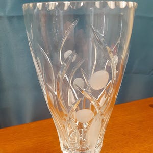 May include: A clear glass vase with a flared shape and a scalloped rim. The vase features etched floral and circular designs. The vase is made of clear glass and is suitable for displaying flowers or as a decorative piece.