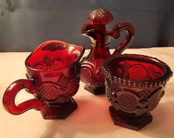 Avon deep ruby 1876 Cape Cod cream & sugar and cruet set. Cruet is 5.5" tall. All in excellent condition with Avon mark on base. Sold as set