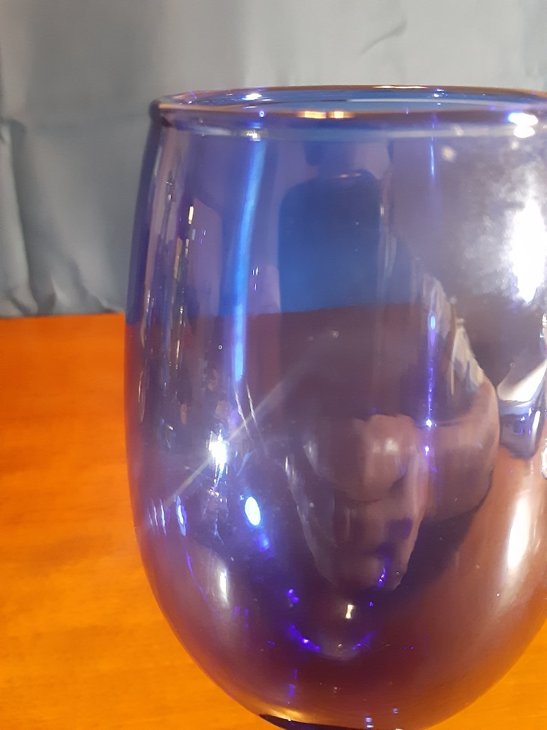 May include: A cobalt blue glass goblet with a rounded base and a wide bowl. The glass is clear and reflects light.