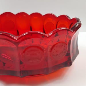 May include: A vibrant red glass bowl with a scalloped rim and geometric sides. The bowl features embossed circular designs and a rich, glossy finish, perfect for serving or display.
