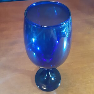 May include: A cobalt blue glass goblet with a wide bowl and a stem. The goblet is empty and sitting on a wooden surface.