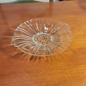 May include: A clear glass bowl with a fluted design and two handles. The bowl is sitting on a wooden table.
