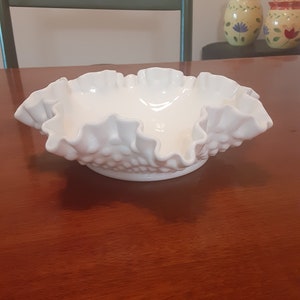 May include: A white, ruffled glass bowl with a textured surface. The bowl is made of milk glass and has a scalloped edge.