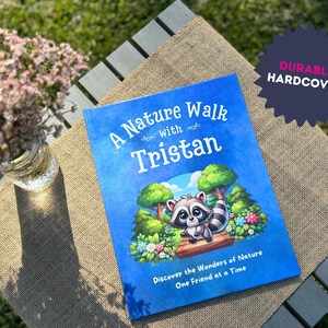 May include: A blue hardcover book with the title "A Nature Walk with Tristan" and an illustration of a raccoon in a forest setting. The book is on a brown burlap surface.