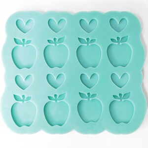 May include: A teal silicone mold with 12 cavities. The cavities are shaped like apples and hearts.
