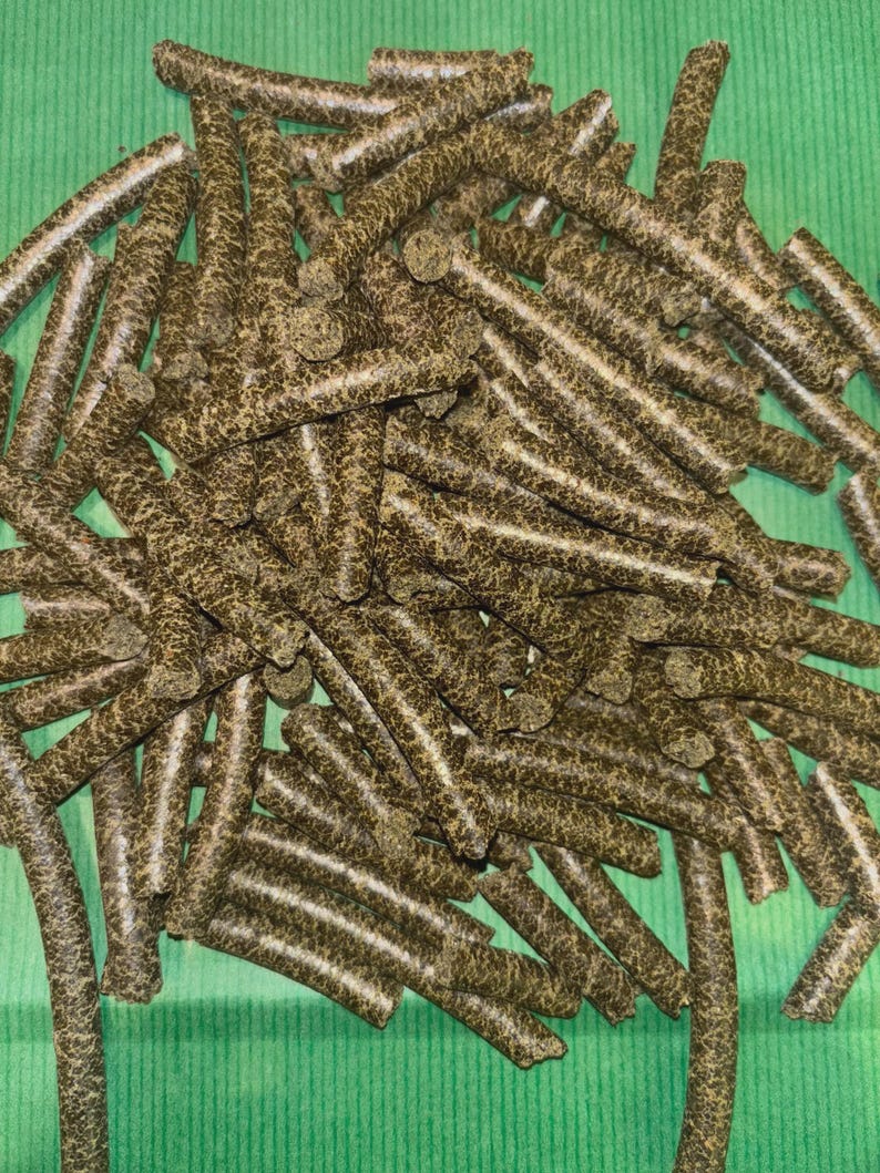May include: A collection of dark brown, cylindrical pellets with a speckled pattern and white lines. The pellets are arranged on a green surface, creating a contrast of colours and textures. The image is a close-up shot.