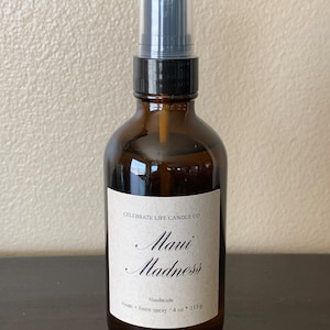 May include: A brown glass bottle with a black spray nozzle and a white label that reads "Celebrate Life Candle Co. Maui Madness Handmade room + linen spray / 4 oz * 113 g"